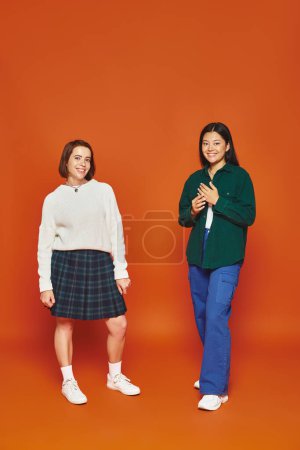 fröhliche junge multikulturelle Freunde in lebendiger Kleidung stehen zusammen auf orangefarbenem Hintergrund
