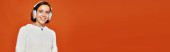 cheerful woman in white sweater and wireless headphones listening music on orange backdrop, banner magic mug #687613496