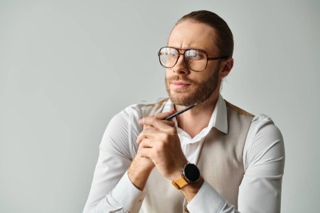 Foto de Guapo modelo masculino concentrado con barba y gafas posando con pluma en la mano y mirando hacia otro lado - Imagen libre de derechos