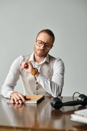 schöner junger Mann mit Bart und Brille schaut auf seine Armbanduhr, während er im Büro hart arbeitet