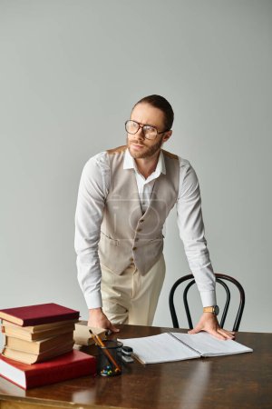 Foto de Joven concentrado con barba y gafas mirando hacia otro lado mientras posa al lado de la mesa en la oficina - Imagen libre de derechos