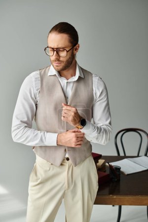 Foto de Buen aspecto joven barbudo modelo masculino con gafas y reloj de pulsera mirando hacia otro lado mientras está en la oficina - Imagen libre de derechos