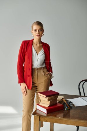 mujer joven de buen aspecto en chaqueta roja posando con la mano en el bolsillo y mirando a la cámara en la oficina