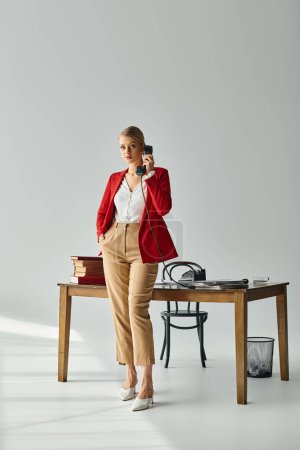 attraktive junge Frau in lebendiger Kleidung posiert mit der Hand in der Tasche, während sie per Retro-Telefon spricht