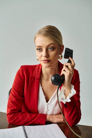 gut aussehende blonde Frau in roter stylischer Jacke, die während ihrer Arbeit im Büro per Vintage-Telefon spricht