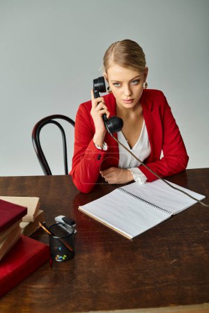 Photo for Beautiful blonde woman in red elegant jacket talking by retro phone while working at office - Royalty Free Image