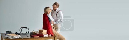 Foto de Sexy joven pareja en elegante atuendos besándose en la mesa y mirando el uno al otro, asunto de trabajo, bandera - Imagen libre de derechos