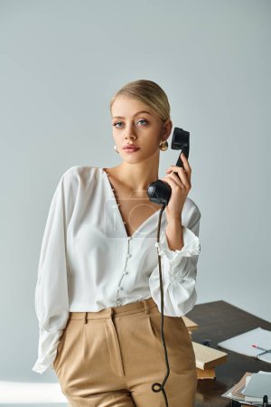attractive young woman with blonde collected hair talking by retro phone and looking at camera