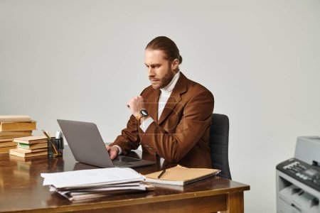 schöner nachdenklicher Mann mit Bart und Armbanduhr in eleganter Jacke bei der Arbeit an seinem Laptop im Büro