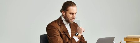 Konzentrierter Mann mit Bart und Armbanduhr in eleganter Jacke bei der Arbeit an seinem Laptop im Büro