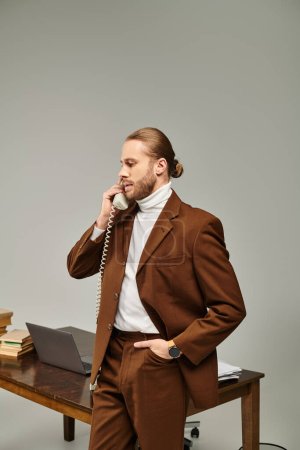 handsome young male model in brown stylish jacket talking by vintage phone with hand in pocket