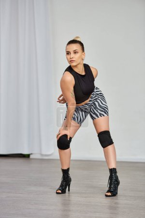 Die gleichgewichtige und anmutige Tänzerin posiert und zeigt Bewegungen in High Heels gegen die weiße Wand