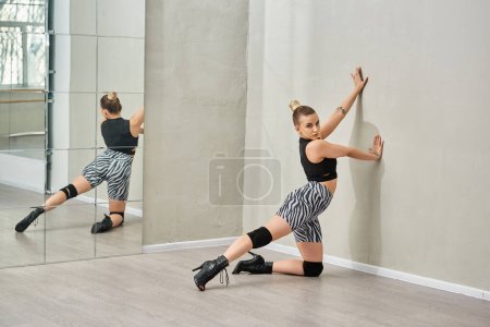 young dancer in zebra shorts and high heels stretches her leg against a wall, choreography