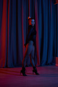 A confident woman strikes a dramatic pose in fishnet stockings, against backdrop of theater curtain puzzle #689818826