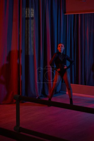 Performerin posiert heftig in ihrem schwarzen Trikot und Netzstrumpfhosen, umrahmt von einem Vorhang