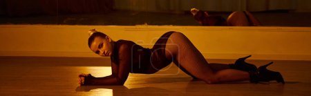 estandarte de la mujer en tacones altos estirando su cuerpo sobre el piso pulido en el estudio de baile