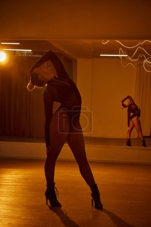 A graceful dancer in black leotard and fishnet tights moves fluidly across the indoor floor
