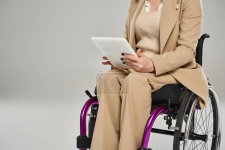 Téléchargez les photos : Vue recadrée de la femme handicapée en fauteuil roulant dans des vêtements élégants tenant tablette, déficience - en image libre de droit