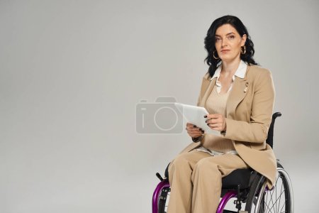 attractive disabled woman in wheelchair wearing pastel attire holding tablet and looking at camera