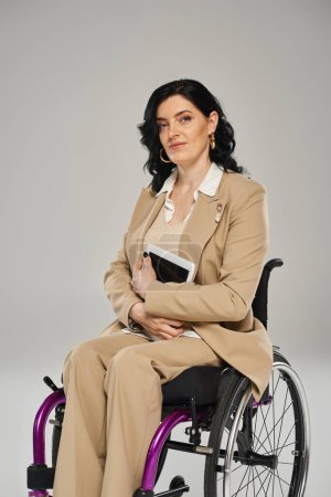 attractive woman with impairment sitting in wheelchair and looking at camera with tablet in hands