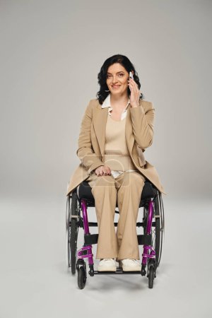 cheerful attractive woman with impairment in wheelchair talking by phone and looking at camera