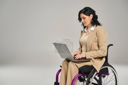 hermosa mujer discapacitada con confianza en silla de ruedas con traje de pastel y trabajando en su computadora portátil