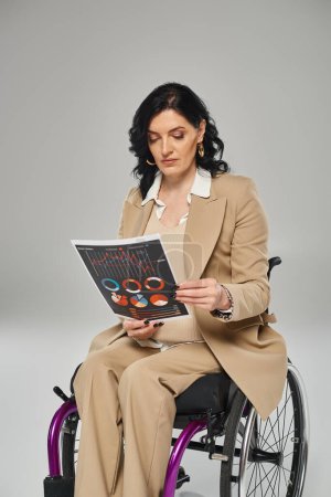 brunette woman with mobility disability in pastel suit looking at graphics while in wheelchair