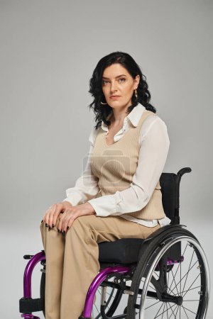 attraktive brünette behinderte Frau in pastellfarbener schicker Kleidung im Rollstuhl blickt direkt in die Kamera