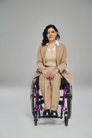 Selbstbewusste Frau mit Gehbehinderung im schicken Anzug sitzt im Rollstuhl und blickt in die Kamera