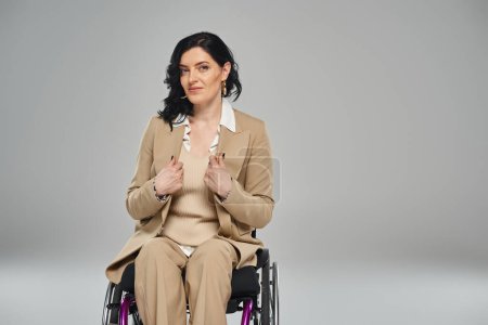 Foto de Mujer confiada con discapacidad en traje elegante pastel sentado en silla de ruedas y mirando a la cámara - Imagen libre de derechos