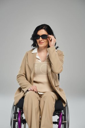 Foto de Alegre hermosa mujer con discapacidad en silla de ruedas con gafas de sol y mirando a la cámara - Imagen libre de derechos