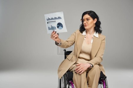 Téléchargez les photos : Chère belle femme avec un handicap de mobilité dans les lunettes regardant des graphiques en fauteuil roulant - en image libre de droit