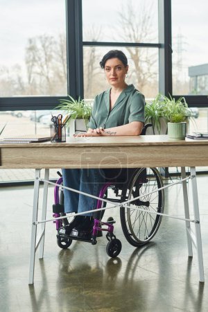 Téléchargez les photos : Belle femme d'affaires handicapée avec tatouage assis en fauteuil roulant tout en travaillant dans son bureau - en image libre de droit