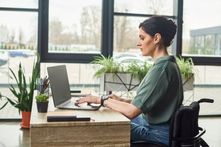 confident hard working businesswoman in casual attire in wheelchair working on laptop in office