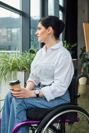 Téléchargez les photos : Belle femme d'affaires gaie en tenue décontractée en fauteuil roulant tenant café tandis que dans le bureau - en image libre de droit