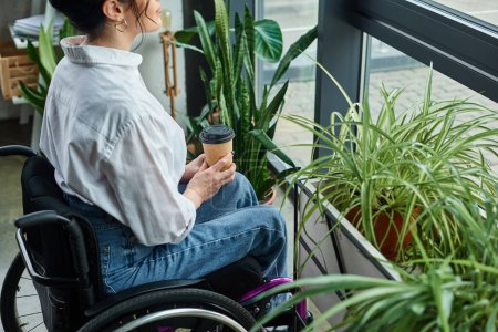 abgeschnittene Ansicht einer behinderten Geschäftsfrau in stylischer Kleidung im Rollstuhl mit Kaffeetasse im Büro