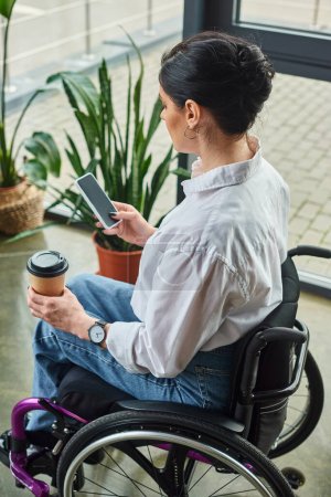 attraktive engagierte Frau mit Behinderung im Rollstuhl in eleganter Kleidung mit Kaffee und Telefon