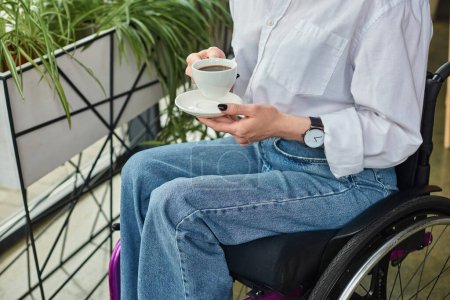 cropped view of businesswoman with mobility disability in wheelchair holding coffee cup in office