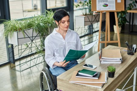 confident disabled businesswoman in wheelchair looking at her paperwork at her workplace in office