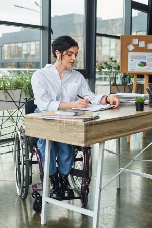 gut aussehende, hart arbeitende Geschäftsfrau mit Behinderung im Rollstuhl macht sich am Tisch Notizen