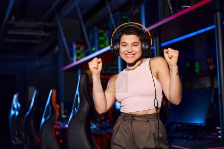 tattooed and happy young woman wearing headphones and holding her fists up, positivity and dance