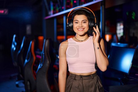 Una joven irradia alegría mientras escucha música a través de sus auriculares en el club de ciberdeporte