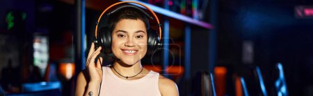 Una mujer joven irradia alegría mientras escucha música a través de sus auriculares en el club de ciberdeporte, pancarta