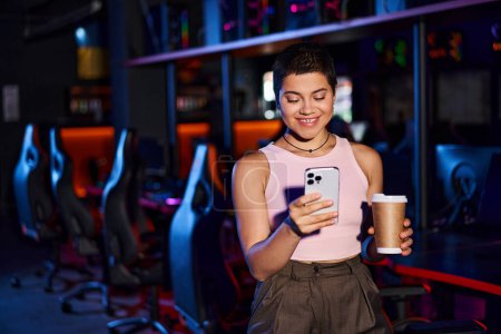 stylish woman, clad in fashionable clothing, smiles as she holds her phone and a cup of coffee