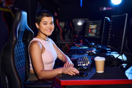 glückliche Frau im Zoomalter, die an einem Schreibtisch mit Computermonitor und Tasse Kaffee sitzt, Cybersport-Spiele