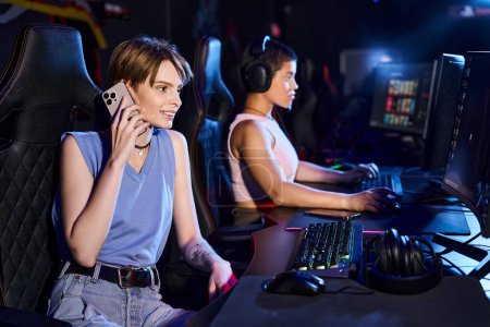 woman sitting at a computer desk talking by phone near friend playing in computer game in club