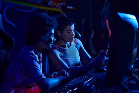 zwei interrassische Frauen, die sich mit Spielen in einem neonbeleuchteten Raum, Cybersport und Gaming-Konzept beschäftigen