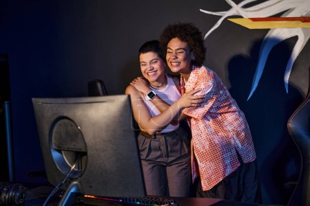 interracial and happy friends hugging and celebrating victory in gaming room, cybersport game