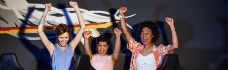 femmes heureuses multiculturelles regardant moniteur d'ordinateur et célébrant la victoire, bannière mains levées