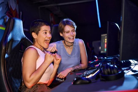 excited women with tattoos concentrating on a cybersport game in computer club room, female gamers